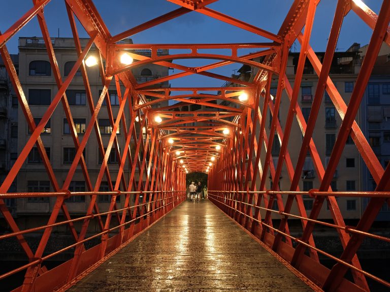 Interior del pont de ferro vermell de les Peixateries Velles, il·luminat al vespre